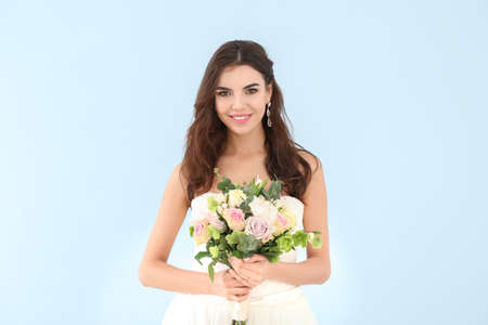 Beautiful young bride with bouquet of flowers on color background