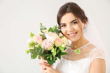Beautiful young bride with bouquet of flowers on light backgroundの写真素材