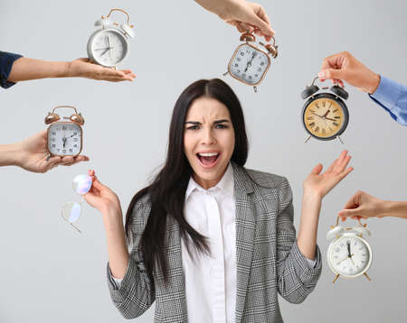 Stressed young businesswoman and hands with alarm clocks on gray background. Deadline conceptの写真素材