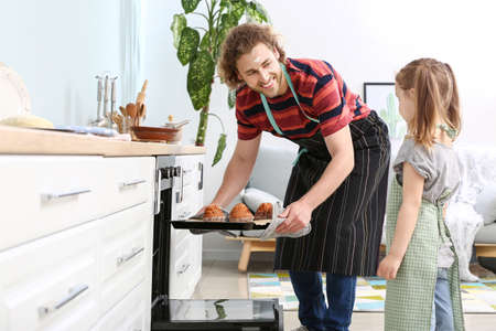 Young man and his little daughter baking tasty muffins at homeの写真素材