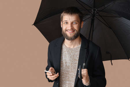 Handsome man with umbrella and mobile phone on color backgroundの写真素材