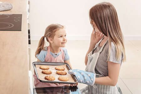 Little girl and her mother baking cookies in kitchen