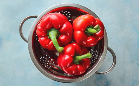 Colander with ripe red peppers on color background