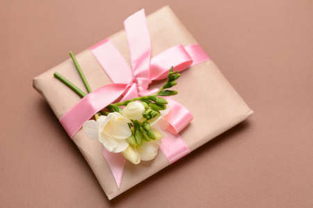 Gift with beautiful freesia flowers on color background