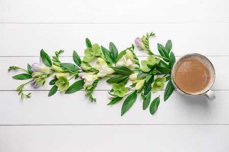 Beautiful flowers and cup of coffee on white wooden background