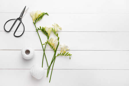 Beautiful freesia flowers, scissors and thread on white wooden tableの写真素材