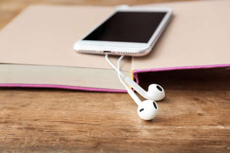 Book, mobile phone and modern earphones on wooden background, closeup. Concept of audiobookの写真素材