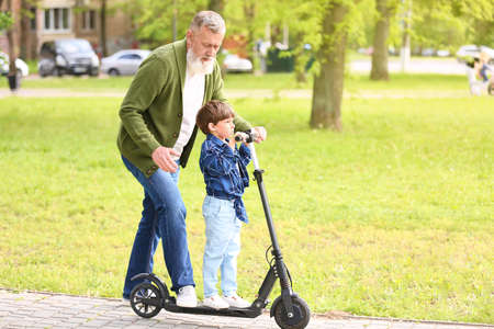 Cute little boy with grandfather riding kick scooter in parkの写真素材