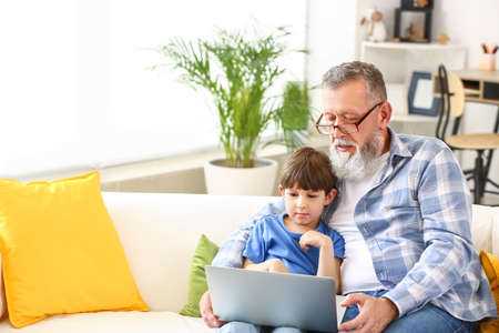 Cute little boy and his grandfather with modern laptop at homeの写真素材