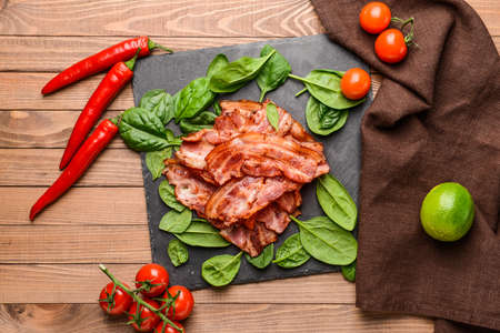 Slate plate with fried bacon on wooden tableの写真素材