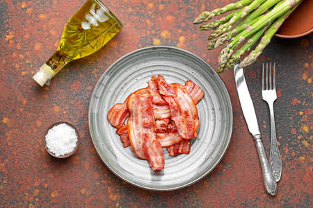 Plate with fried bacon on color background
