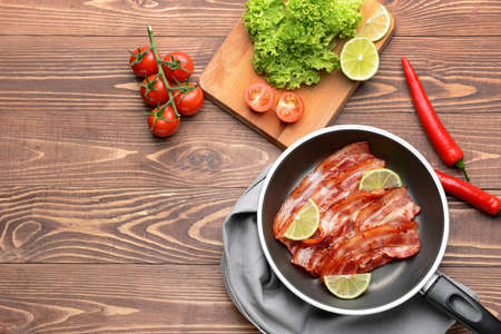 Frying pan with cooked bacon on wooden tableの写真素材