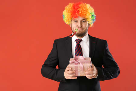 Funny businessman in rainbow wig and with gift on color backgroundの写真素材