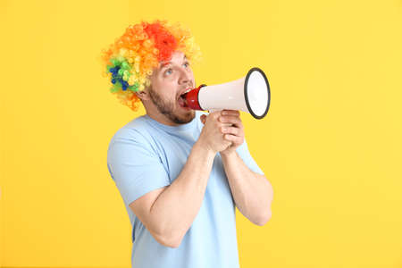Funny man in wig and with megaphone on color background