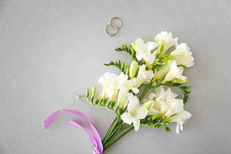 Wedding rings and beautiful freesia flowers on light background