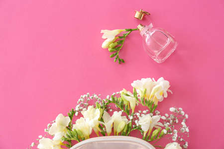 Cosmetic bag with beautiful freesia flowers and perfume on color background