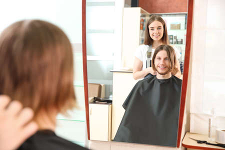 Reflection of female hairdresser working with client in salonの写真素材