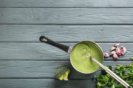 Saucepan with delicious broccoli cream soup on wooden table