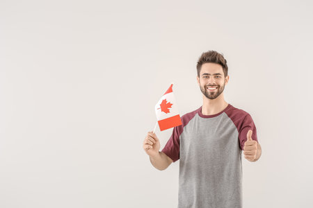 Young man with Canadian flag on light backgroundの写真素材