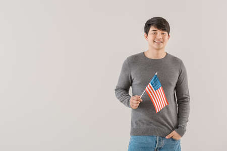 Young Asian man with USA flag on light background