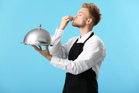 Handsome male chef with tray and cloche on color background
