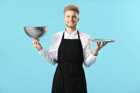 Handsome male chef with tray and cloche on color backgroundの写真素材