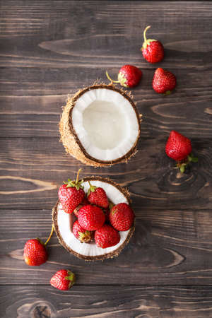 Coconut with ripe red strawberry on wooden background