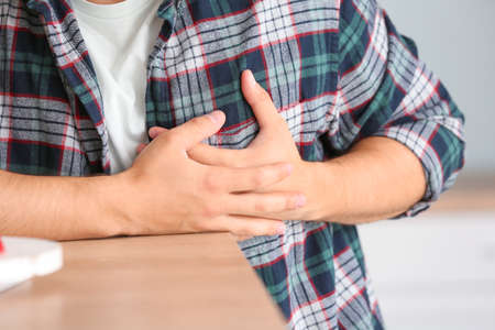 Young man suffering from heart attack at home, closeup