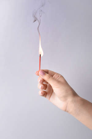 Female hand with burning match on light backgroundの写真素材