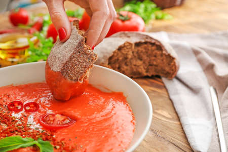 Woman dipping bread into bowl with tasty cream soup, closeupの写真素材