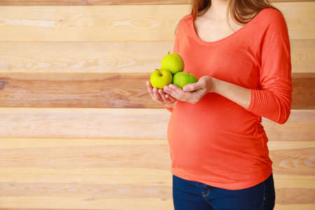 Beautiful pregnant woman with apples on wooden backgroundの写真素材