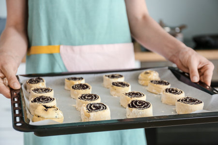 Woman holding raw poppy buns on baking sheet in kitchen