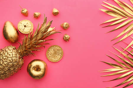 Golden tropical leaves and fruits on color background
