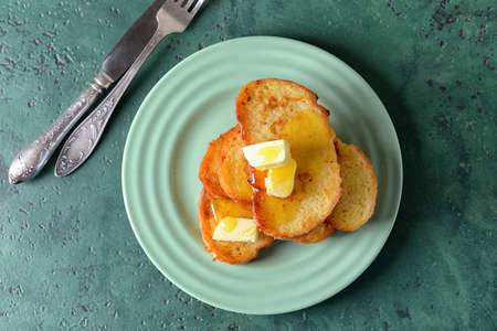 Plate with tasty French toasts and butter on color background