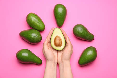 Female hands and ripe avocados on color background