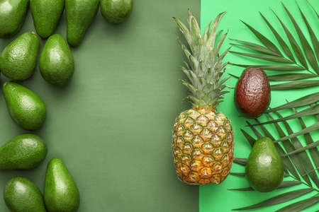 Fresh avocados, pineapple and palm leaves on color backgroundの写真素材