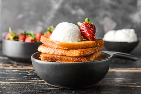 Frying pan with tasty French toasts, ice cream and strawberry on dark table