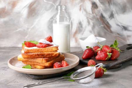 Plate with tasty French toasts and strawberry on gray table