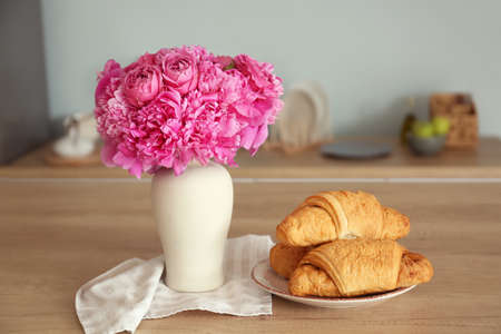 Vase with beautiful peonies and croissants on wooden tableの写真素材