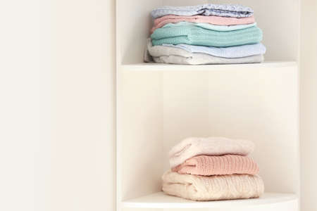Rack with stacks of clean clothes near white wall
