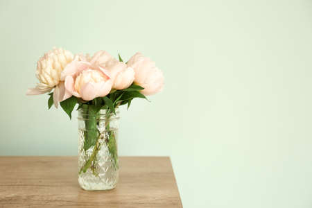 Vase with beautiful peony flowers on table against color backgroundの写真素材