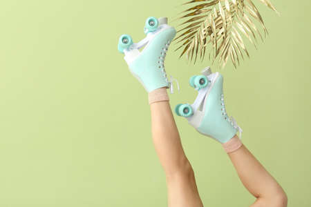 Legs of woman in roller skates and golden tropical leaves on color background