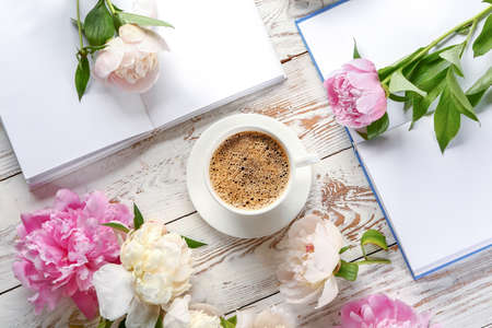Cup of coffee with peonies and books on white table
