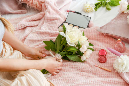 Young woman with bouquet of beautiful peonies sitting on bedの写真素材