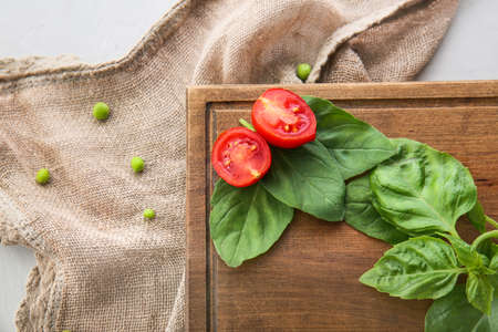 Wooden board with fresh basil leaves and vegetables on tableの写真素材