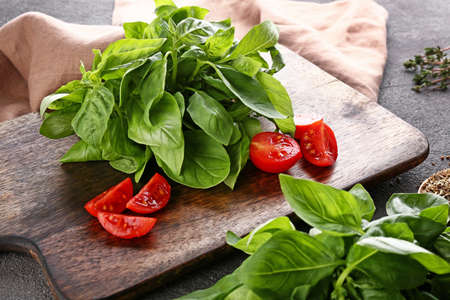 Cutting board with tomatoes and fresh basil on tableの写真素材