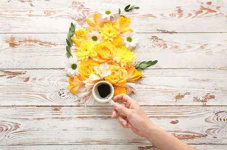 Female hand with cup of coffee and beautiful flowers on wooden backgroundの写真素材