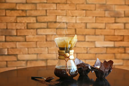 Jar with hot coffee on table against brick background