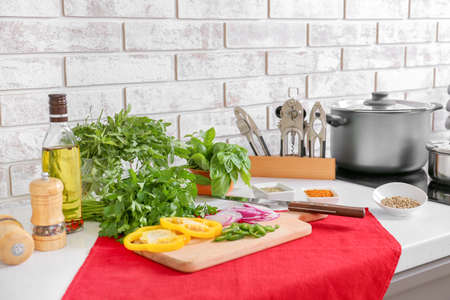 Cutting board with fresh herbs, vegetables, oil and spices on table in kitchen
