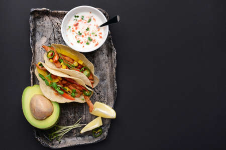 Plate with tasty fresh tacos and sauce on dark background